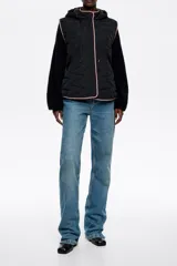 Chaleco acolchado negro de corte recto con capucha integrada, cierre frontal de botones a presión ocultos y vivos en color rosado a contraste.