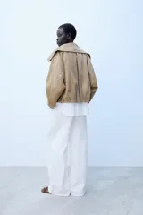 Cazadora bomber marrón de efecto gamuza, con cuello de solapa amplia, manga larga, bolsillos delanteros y cierre frontal asimétrico con cremallera metálica.