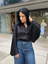Blusa negra de manga larga con cuello camisero y puños acampanados o con aberturas.
