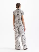 Pantalón de punto de tiro alto, pierna ancha y cintura elastizada. Presenta un estampado integral en tonos grises y negros sobre fondo beige claro, con motivos de cerezas, figuras estilizadas y cadenas.