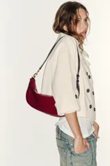 Bolso de hombro de diseño semicircular, confeccionado en material sintético efecto charol de color rojo. Cuenta con una correa ajustable fina con detalles metálicos dorados y cierre superior con cremallera.