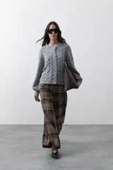 Cardigan de tejido de punto color marrón chocolate, con diseño de trenzas en el frente y mangas. Presenta cuello redondo, cierre frontal con botones al tono y puños acanalados.