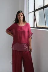 Blusa de seda color bordó con diseño holgado, cuello redondo y mangas cortas tipo kimono. Presenta un panel frontal inferior y detalles en las mangas con lentejuelas al tono.