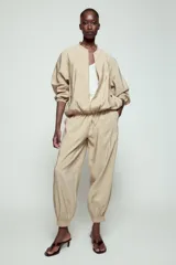 Pantalón satinado de tiro alto color beige, con cintura elástica ajustable con cordones, bolsillos delanteros y puños elásticos en los tobillos.