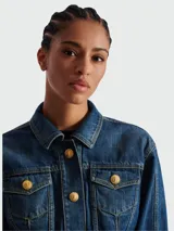 Chaqueta de jean corta azul con efecto desgastado, cuello clásico, cierre frontal con botones dorados y bolsillos con solapa en el pecho.