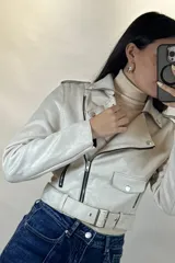 Chaqueta corta tipo biker confeccionada en gamuza color beige, con cierre frontal cruzado, solapas amplias, bolsillos con cierre y cinturón ajustable en la cintura.