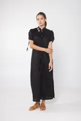 Túnica larga negra de lino con cuello mao, mangas cortas abullonadas con lazos y cierre frontal con botones.