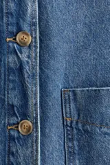 Campera camisera en denim rígido con cuello, cierre frontal de botones, puños abotonados, bolsillos de parche delanteros y dobladillo redondeado.