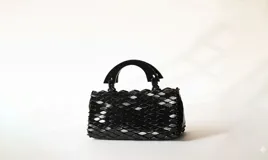 Cartera compacta de mano color negro con diseño texturizado en relieve similar a escamas y asas rígidas de madera.