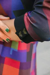 Vestido corto con estampado geométrico en tonos violeta, rojo y negro, confeccionado en jersey elastizado con efecto gamuzado. Presenta cuello redondo y mangas 3/4 con puños abotonados. La falda es de corte irregular con volados.