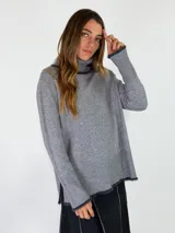 Sweater de cuello alto en color beige, con diseño de punto liso y terminaciones acanaladas en puños y ruedo. Presenta aberturas laterales en el bajo y un detalle de borde desflecado en el ruedo y los puños.