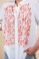 Camisa blanca de manga larga con diseño pintado a mano por Carolina De Cunto, con trazos abstractos en tonos rojo, naranja y rosa. Presenta cuello camisero y cierre frontal de botones.