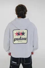 Canguro gris oscuro con efecto lavado (acid wash) y capucha. Presenta un pequeño estampado frontal con estrellas y la palabra "pulau" en tonos rosado y amarillo. Tiene bolsillo canguro y puños acanalados.