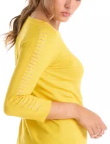 Buzo de tejido fino en color blanco, con cuello redondo y mangas tres cuartos tipo raglán. Presenta un detalle decorativo de tachas metálicas a lo largo de las mangas.