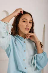 Camisa blanca con estampado de hojas en tonos beige y verde, cuello camisero, mangas largas con lazos en los puños y botones de madera.