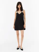 Vestido corto de seda color negro, con escote en V y tirantes decorados con apliques circulares metálicos y nácar. Diseño de corte recto y ligero.