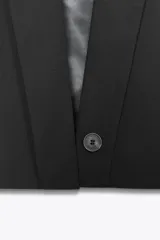 Chaleco corto de Zara con cuello solapa, diseño sin mangas con hombreras y forro interior. Presenta un corte estructurado con cierre frontal mediante botón oculto.