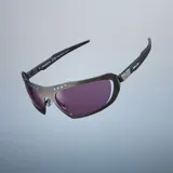 Lentes de sol de diseño envolvente con montura de acero inoxidable en color gunmetal y lentes de nylon color violeta. Presentan un diseño deportivo con detalles perforados en la parte superior del marco y patillas de acetato.