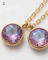 Collar de cadena fina dorada con cinco dijes colgantes redondos de cristal facetado en tono violeta tornasolado.