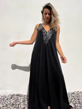Vestido largo de corte holgado en color negro, con escote en V profundo decorado con lentejuelas negras brillantes. Presenta un diseño sin mangas y una caída fluida.