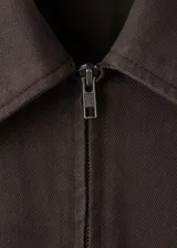 Enterito largo de algodón estilo tejano, color marrón, con cuello camisero, mangas cortas, cierre frontal con cremallera y cinturón ajustable en la cintura.