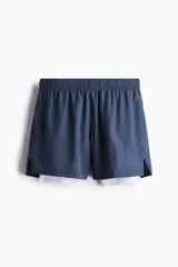 Short deportivo de doble capa con tecnología DryMove, compuesto por un short exterior azul de corte estándar con aberturas laterales y una calza interior blanca integrada con bolsillo lateral. Cuenta con cintura elástica con cordón de ajuste oculto y bolsillos laterales.