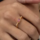 Anillo dorado con piedra central rectangular color borgoña y dos diamantes circulares a cada lado.