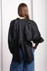 Camisa de lino blanca, de corte oversize, con mangas largas abullonadas, cuello mao y botones. Es más larga en la parte trasera e incluye un tajo en la espalda.