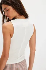 Musculosa blanca de algodón acanalado con escote henley abotonado y costuras visibles en los bordes.