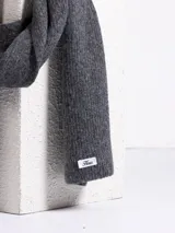 Bufanda de tejido de punto acanalado en color negro, con etiqueta de marca en uno de sus extremos.