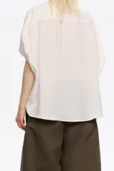 Camisa de manga corta tipo murciélago, con cuello camisero y botones frontales.