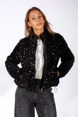 Campera negra con acabado brillante de lentejuelas, cuello alto, cierre frontal y bolsillos laterales con detalles en terciopelo.