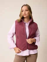 Chaleco de sherpa color bordó con cierre frontal completo, cuello alto y bolsillos laterales con cierre. Presenta un bolsillo adicional con cierre en el pecho y logo bordado.