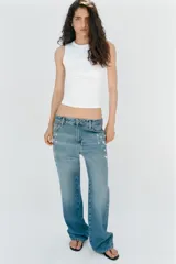 Jeans tiro medio de corte relaxed leg y largo completo, confeccionados en denim azul claro. Presentan detalles de aplicaciones de pedrería y joyas a contraste en los laterales superiores y bolsillos delanteros, estilo clásico de cinco bolsillos y cierre frontal con cremallera y botón metálico.
