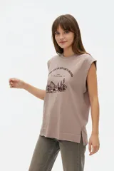 Musculosa color crudo con estampado frontal de paisaje montañoso y texto "EXPLORING Outlands", corte holgado y aberturas laterales en el ruedo.