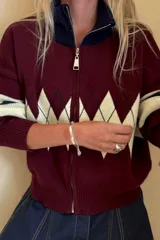Campera tejida de punto con cierre frontal completo y cuello alto. Presenta un diseño con patrón de rombos en la parte central y franjas horizontales en las mangas.