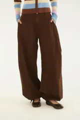 Pantalón ancho de sarga color marrón, de corte holgado y fluido, con bolsillos delanteros y cierre de cremallera y botón.