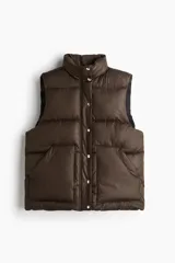Chaleco puffer color marrón oscuro, acolchado, con cuello alto, cierre frontal con botones a presión y bolsillos delanteros tipo parche.