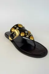 Sandalia plana de gamuza marrón, estilo ojota, con apliques metálicos dorados y hebilla decorativa.