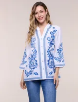 Blusa blanca con bordados florales en azul, de manga tres cuartos y cuello mao con escote en V.
