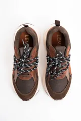 Zapatilla urbana de diseño chunky, combinando paneles de gamuza y cuero en tonos chocolate con malla técnica. Presenta cordones bicolores y una suela de plataforma de goma en color crema.