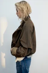 Chaqueta encerada color marrón con efecto lavado, cuello subido y manga larga. Cuenta con bolsillos frontales de plastrón y cierre de cremallera oculto por solapa con botones a presión. Los puños reversibles dejan ver un forro interior con estampado a cuadros.