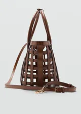 Bolso tipo cesta de color marrón, con diseño trenzado y estructura cuadriculada, asas cortas de mano y correa larga ajustable y desmontable. Incluye charm decorativo y cierre de cremallera.