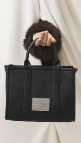 Cartera estructurada de tamaño mediano, confeccionada en símil cuero color negro. Presenta doble asa de mano, correa larga ajustable y desmontable, y un bolsillo trasero con cierre. El compartimento principal cuenta con cierre, división interna y bolsillos organizadores.