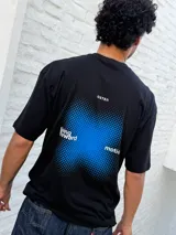 Remera negra de corte oversize con cuello redondo y manga corta. Presenta un pequeño estampado blanco con texto y un cuadrado difuminado azul en el pecho.