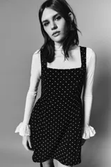Vestido corto negro con estampado de lunares blancos, escote cuadrado, breteles anchos, cuerpo entallado y falda evasé con vuelo.