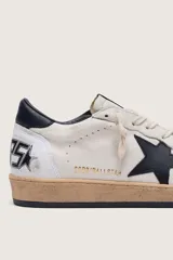 Zapatillas Golden Goose modelo Ball Star, confeccionadas en cuero con efecto desgastado. Diseño en color blanco con estrella lateral en negro, contrafuerte negro y suela de aspecto envejecido.