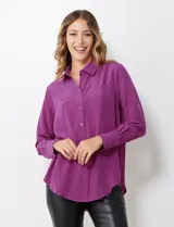 Camisa de satén color violeta, con cuello clásico, cierre frontal con botones, manga larga con puños anchos abotonados y bolsillo aplicado en el pecho.