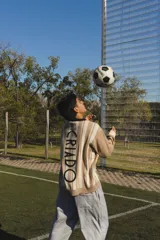 Buzo de punto tejido en jacquard con diseño de rayas verticales en tonos beige y blanco. Presenta cuello polo en color negro, puños y ruedo acanalados en blanco, y bordados alusivos al mundial en el pecho.