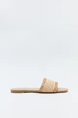 Sandalias planas color beige, con capellada ancha de tejido trenzado con texturas naturales y detalles de hilo contrastante.